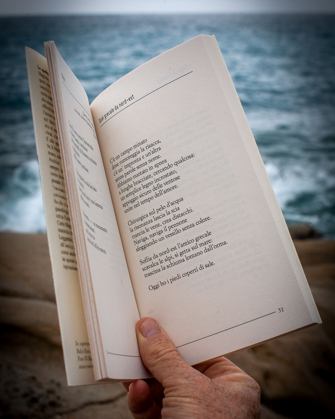 libro in primo piano tenuto aperto da una mano, si legge una poesia
