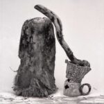 Composizione con pezzo di tronco di palma, radice scortecciata e vecchia caffettiera arrugginita su un ripiano, in bianco e nero.