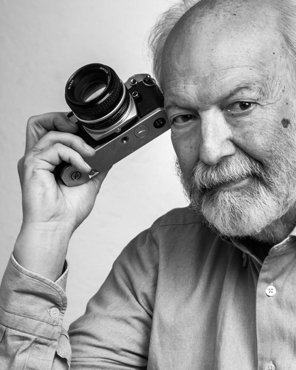 Primissimo piano di uomo anziano con barba bianca che impugna una macchina fotografica
