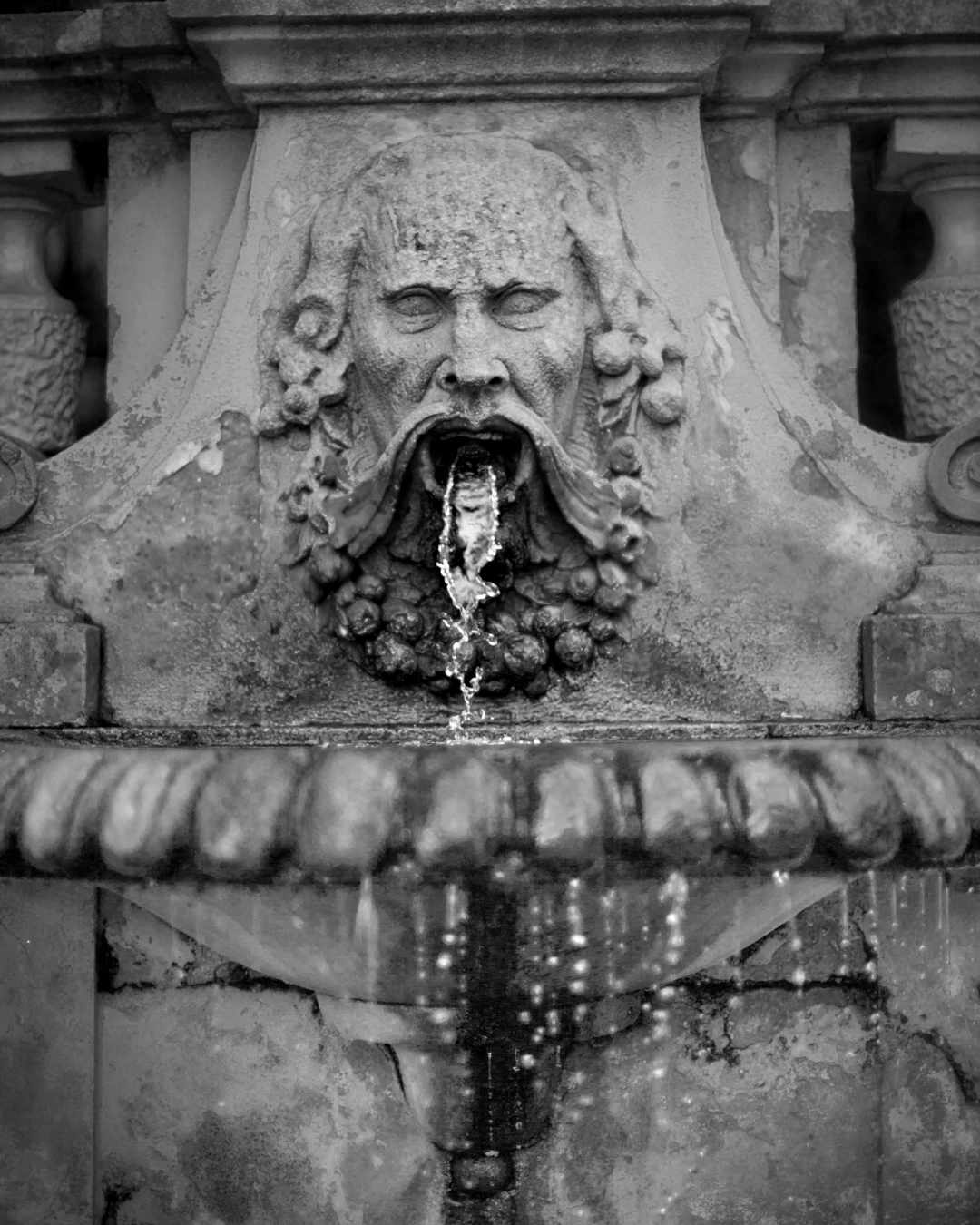 Primo piano di una fontana, scultura di un viso con acqua che esce dalla bocca, fotografia in bianco e nero