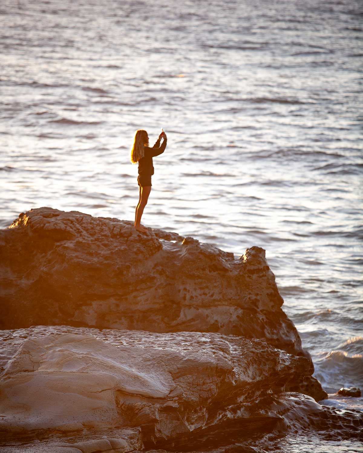 Profilo di donna in piedi su uno scoglio nell'atto di fare un selfie.